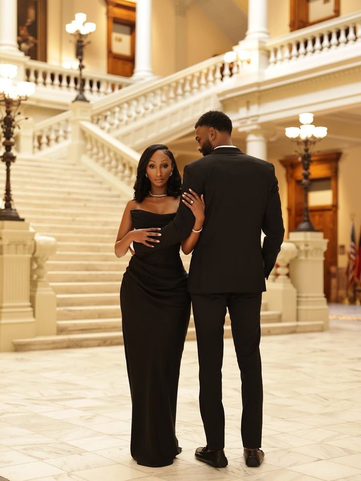 A couple in black formalwear standing in a grand hall